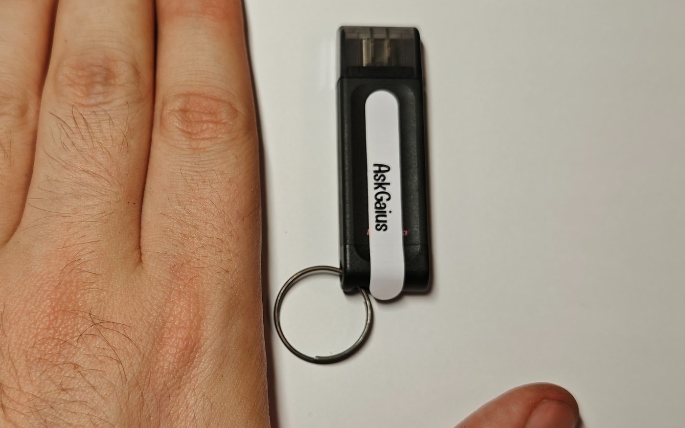 The AskGaius drive on a keyring beside a hand, showing how small it is